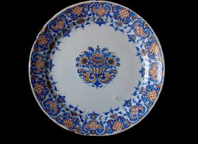 25.5 cm plate in Majolica (faience) a gran fuoco. Rouen, beginning of the 18th century Centre decoration featuring a basket of flowers in blue and ochre, bordered by festoons and lambrequins (mantling). Private Collection