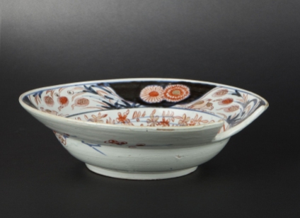 Porcelain barber’s basin with Imari decoration, iron red under glaze and gilded enamel.  The ornamentation depicts two gates and a vase of blooming peonies under a weeping willow. Japan, around 1700. Private Collection.