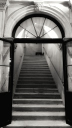 On the right, a grand staircase led to the first floor. An old ceiling lamp cast a yellowish light on the white marble balustrade. On the landing wall, at the end of the first flight of steps, Rosalba could make out two dark canvases hanging over a painted wooden bench. From The Laws of Time, a novel by Andrea Perego Photo ©AndreaPerego